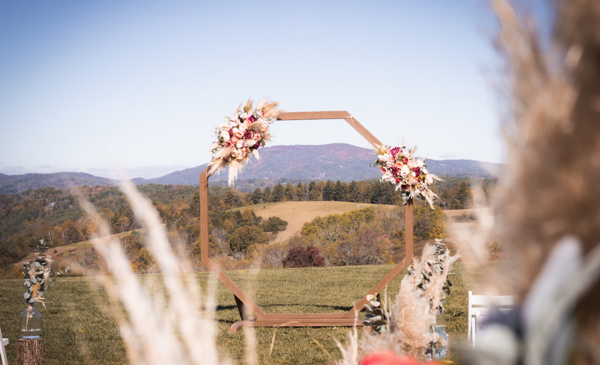 An outdoor ceremony arch dressed in florals, set against rolling mountains at golden hour