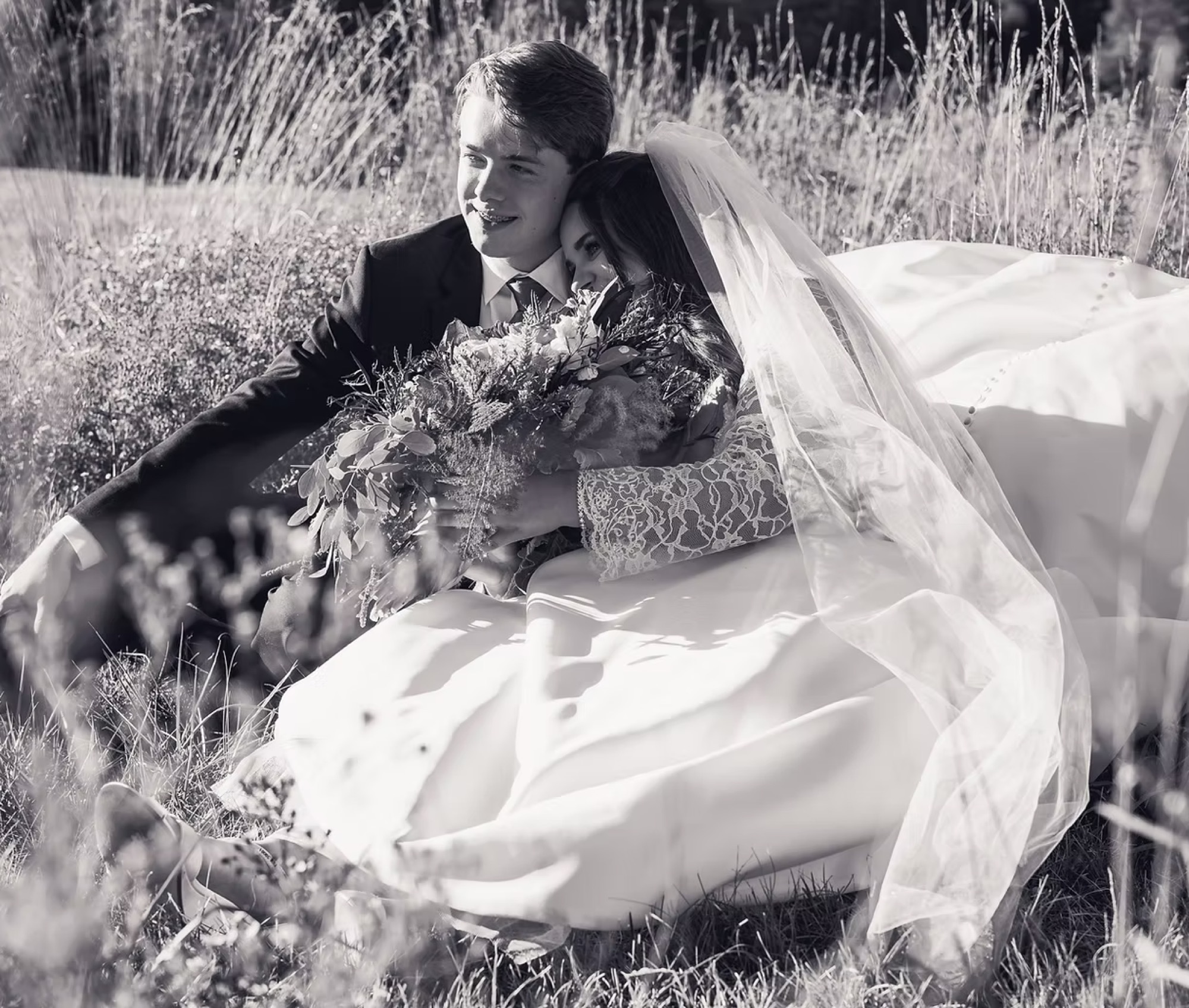 A newly married couple resting together in a wildflower field, photographed in black and white