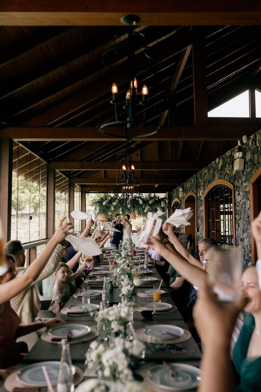 Guests raising napkins in a toast down a long reception table